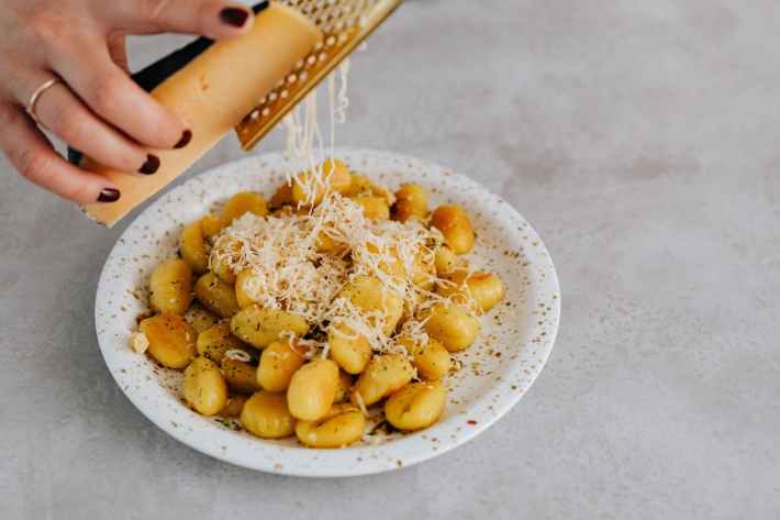 a person grating cheese on a gnocchi