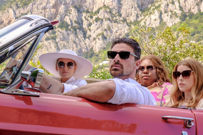 Characters driving in a red convertible with Capri in the background.