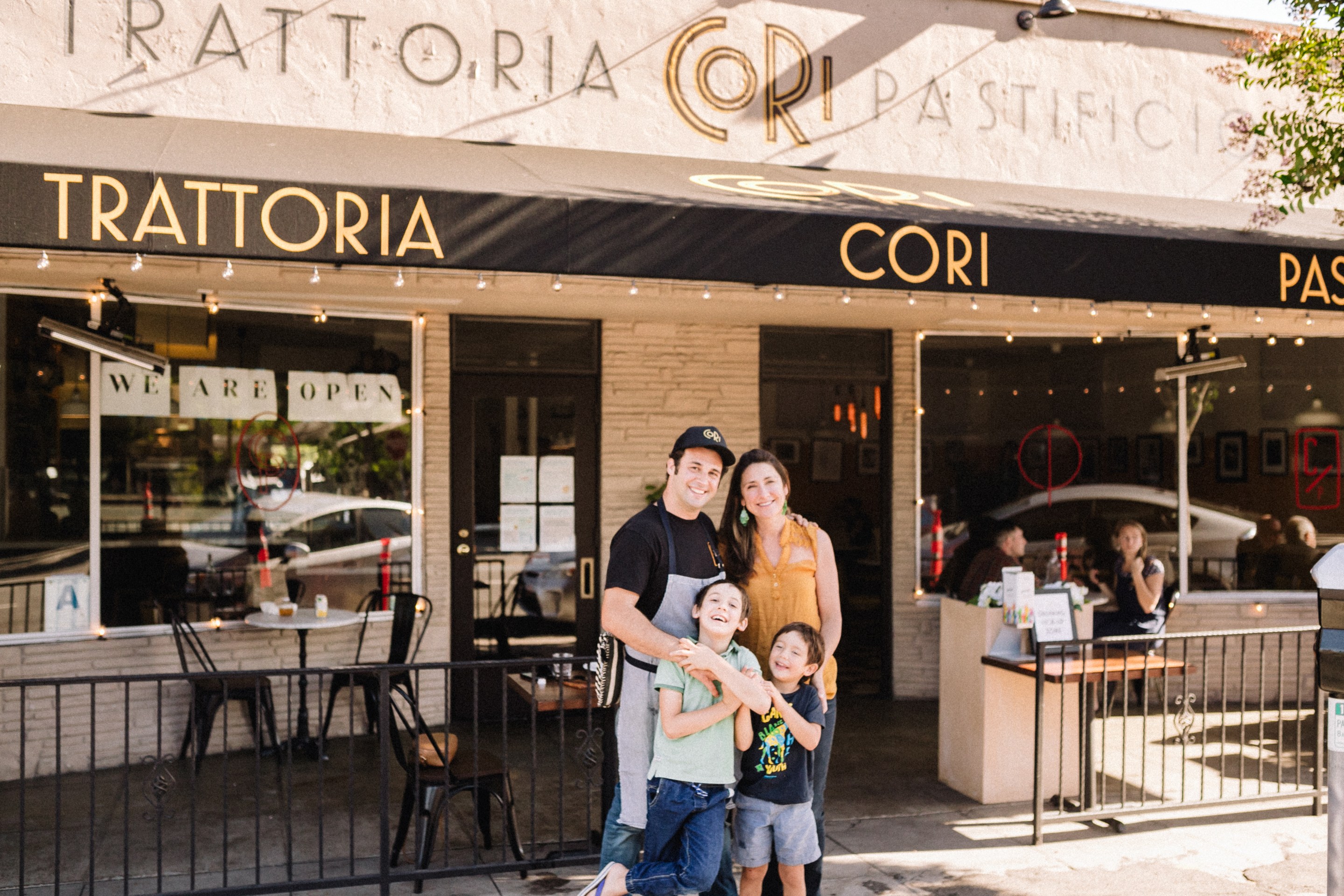 Chef Accursio Lota and his wife, Corinne Goria, pose with their two children in front of Cori Trattoria, the award-winning San Diego restaurant that inspired their next concept, Dora.