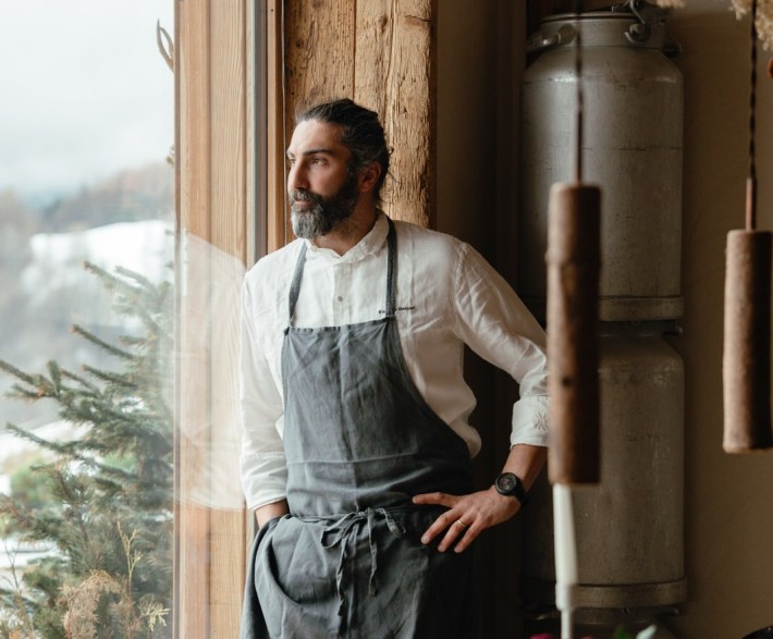 Chef Riccardo Gaspari gazing out a window in his apron, with shoulder-length hair.