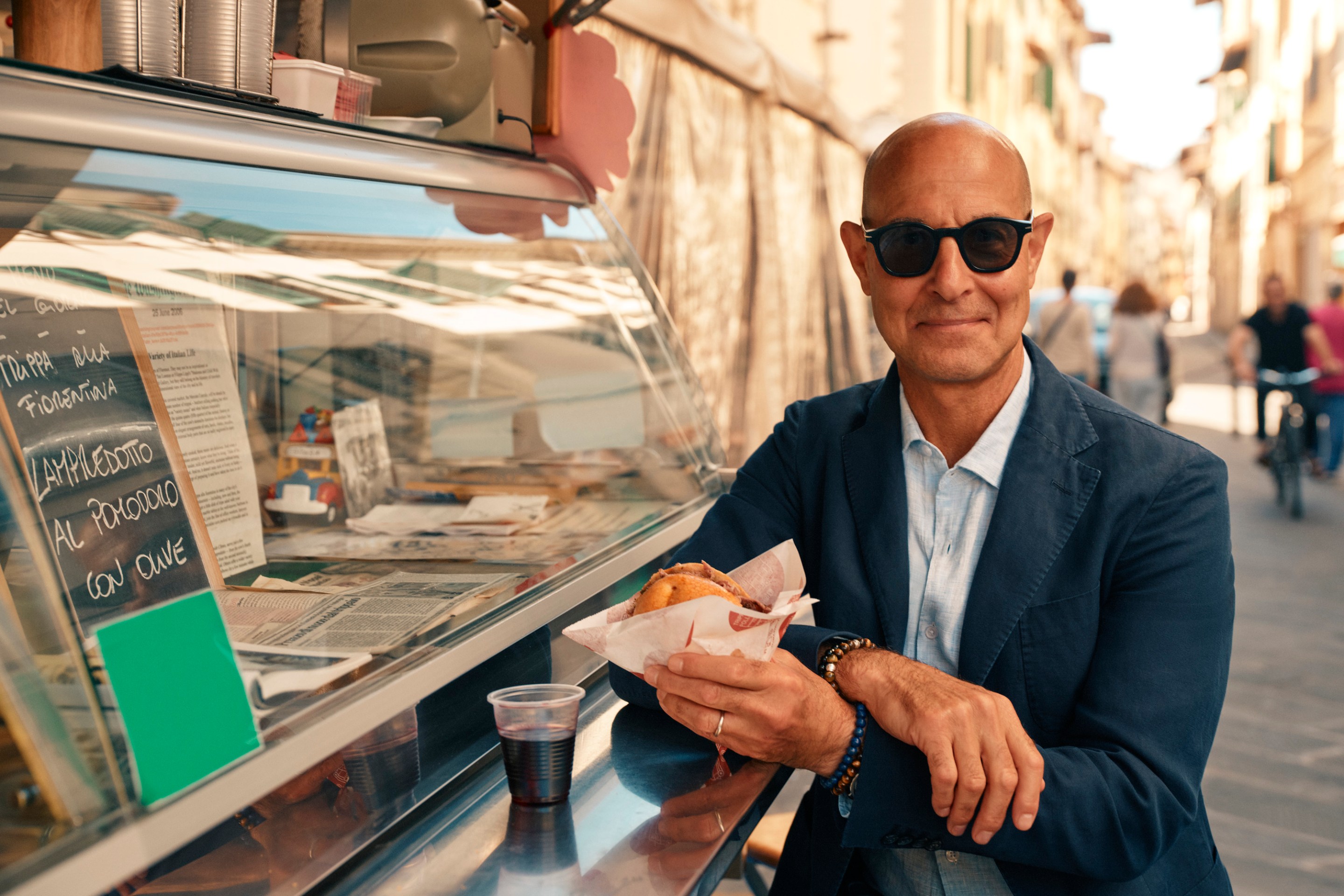 Stanley Tucci enjoys a panino and red wine at a street food stall in Florence.