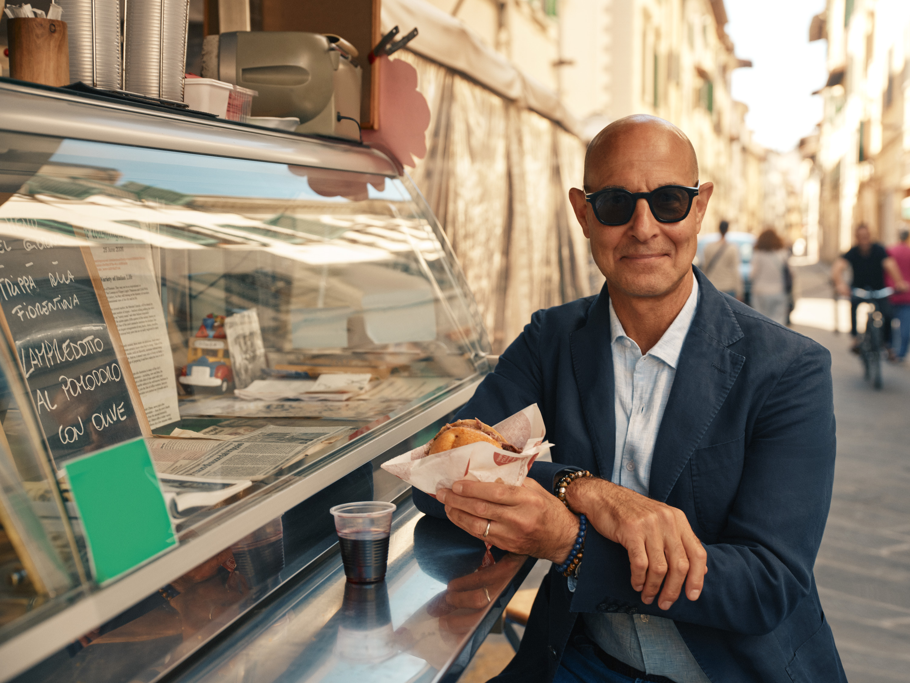 Stanley Tucci enjoys a panino and red wine at a street food stall in Florence.
