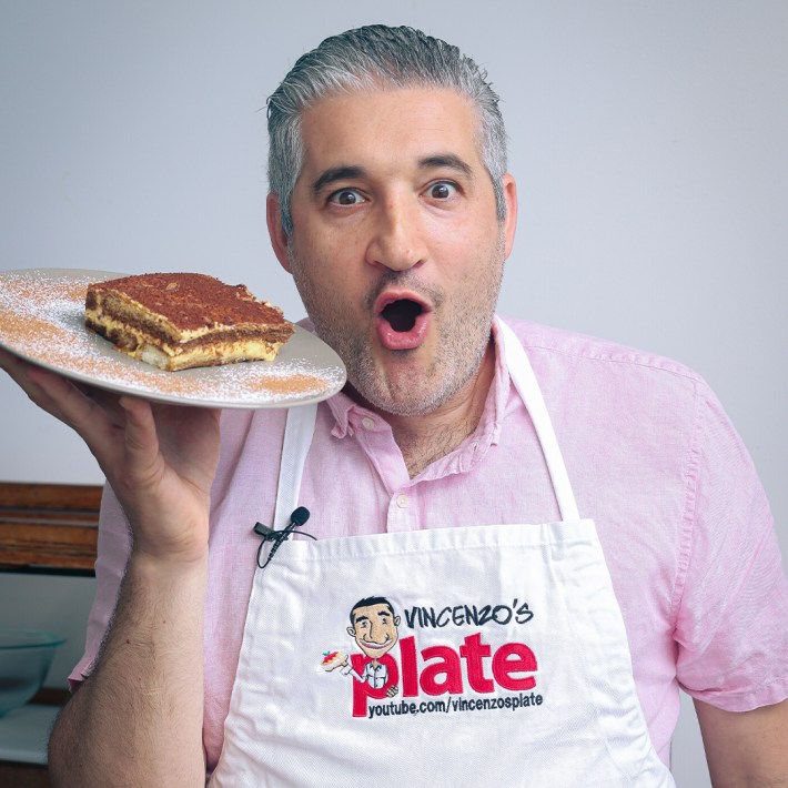 Vincenzo holding a plate of tiramisu with a surprised expression.