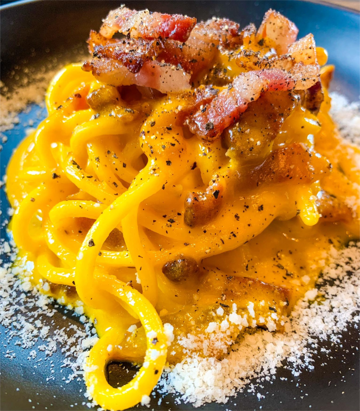 Close-up of NEROLAB’s house-made carbonara, with thick spaghetti, topped with cheese and pancetta.