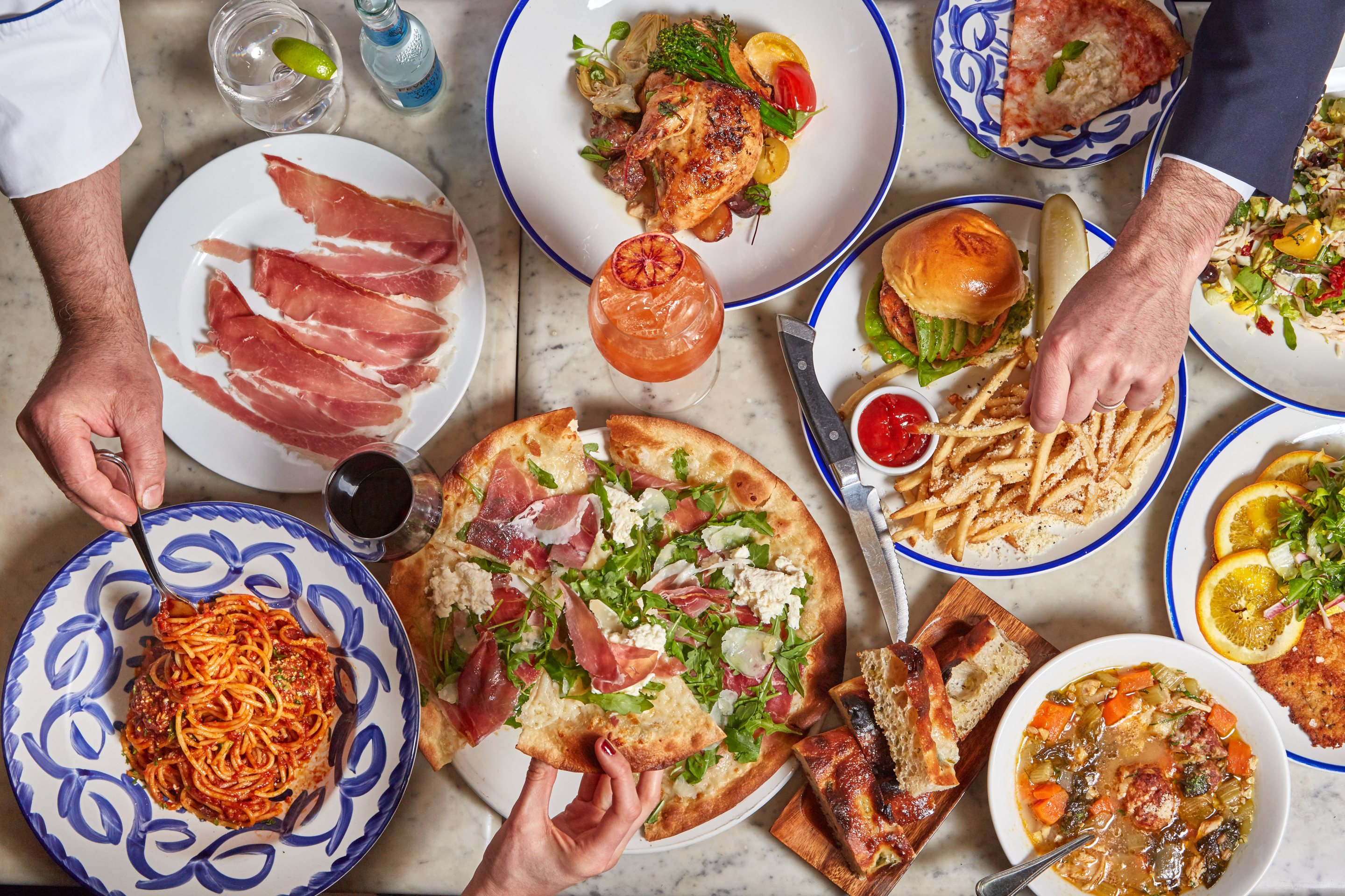 Overhead view of Italian dishes including pizza, pasta, and prosciutto.