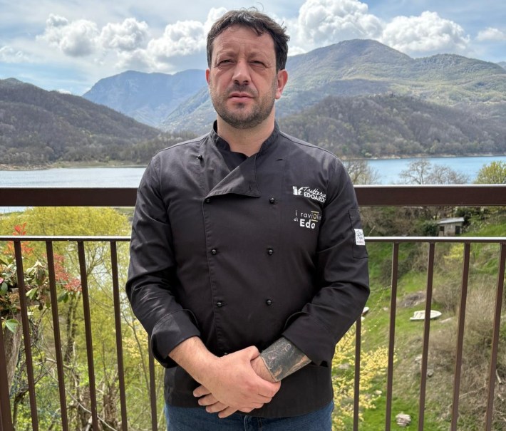 Chef Emiliano Di Leginio standing on a balcony with mountains and a lake in the background.