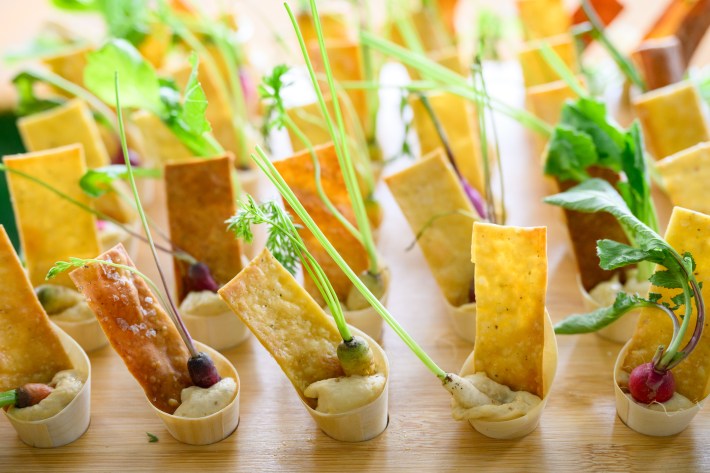 Individual appetizer servings featuring colorful mini carrots and crisp crackers set in small wooden cups with dip, beautifully arranged on a tray.