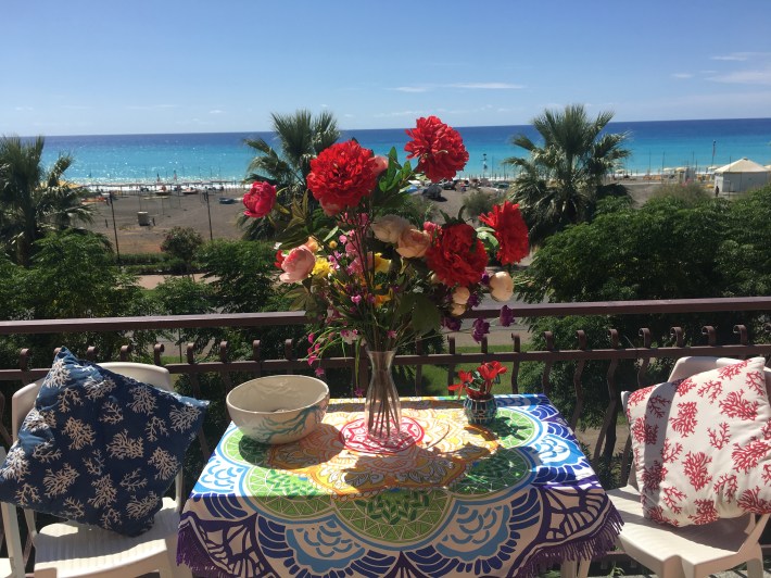 Colorful balcony table with fresh flowers, overlooking Praia a Mare beach and the turquoise sea in Calabria, Italy.