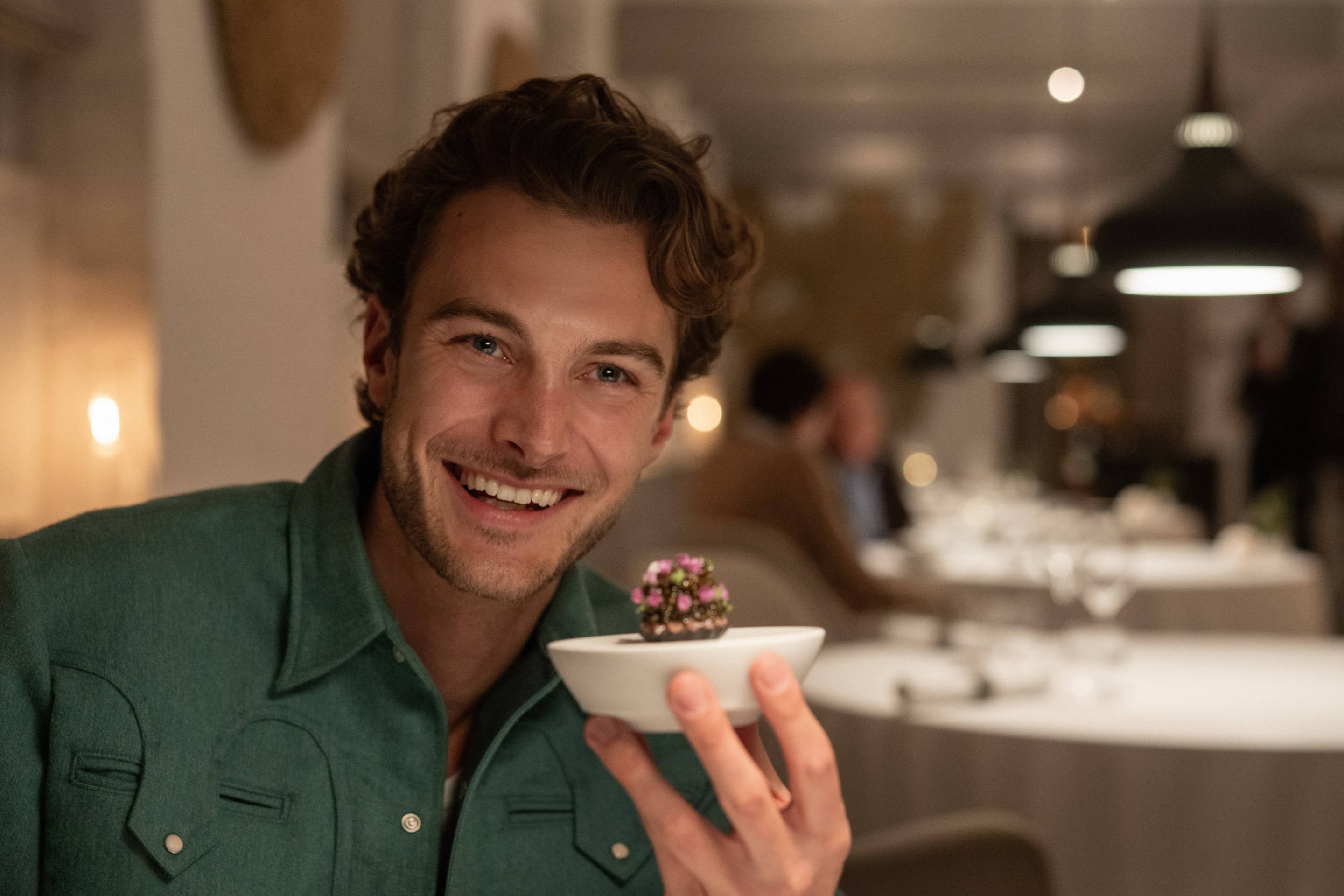Jesse Burgess of Topjaw smiles in a green shirt while holding a small dish in a restaurant.