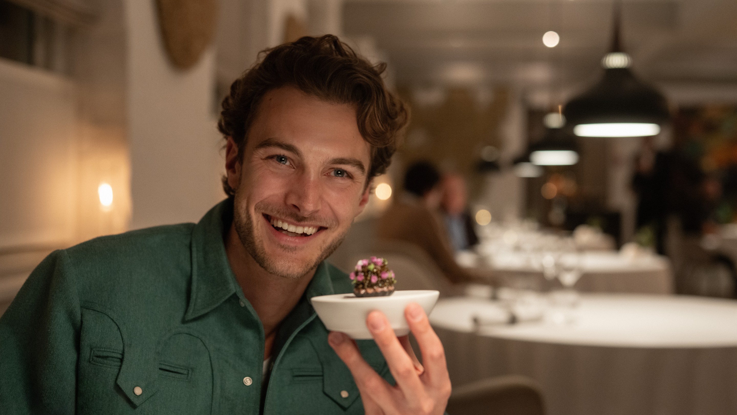 Jesse Burgess of Topjaw smiles in a green shirt while holding a small dish in a restaurant.