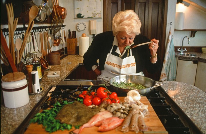 Marcella Hazan tasting food from a wooden spoon in her Venice kitchen.