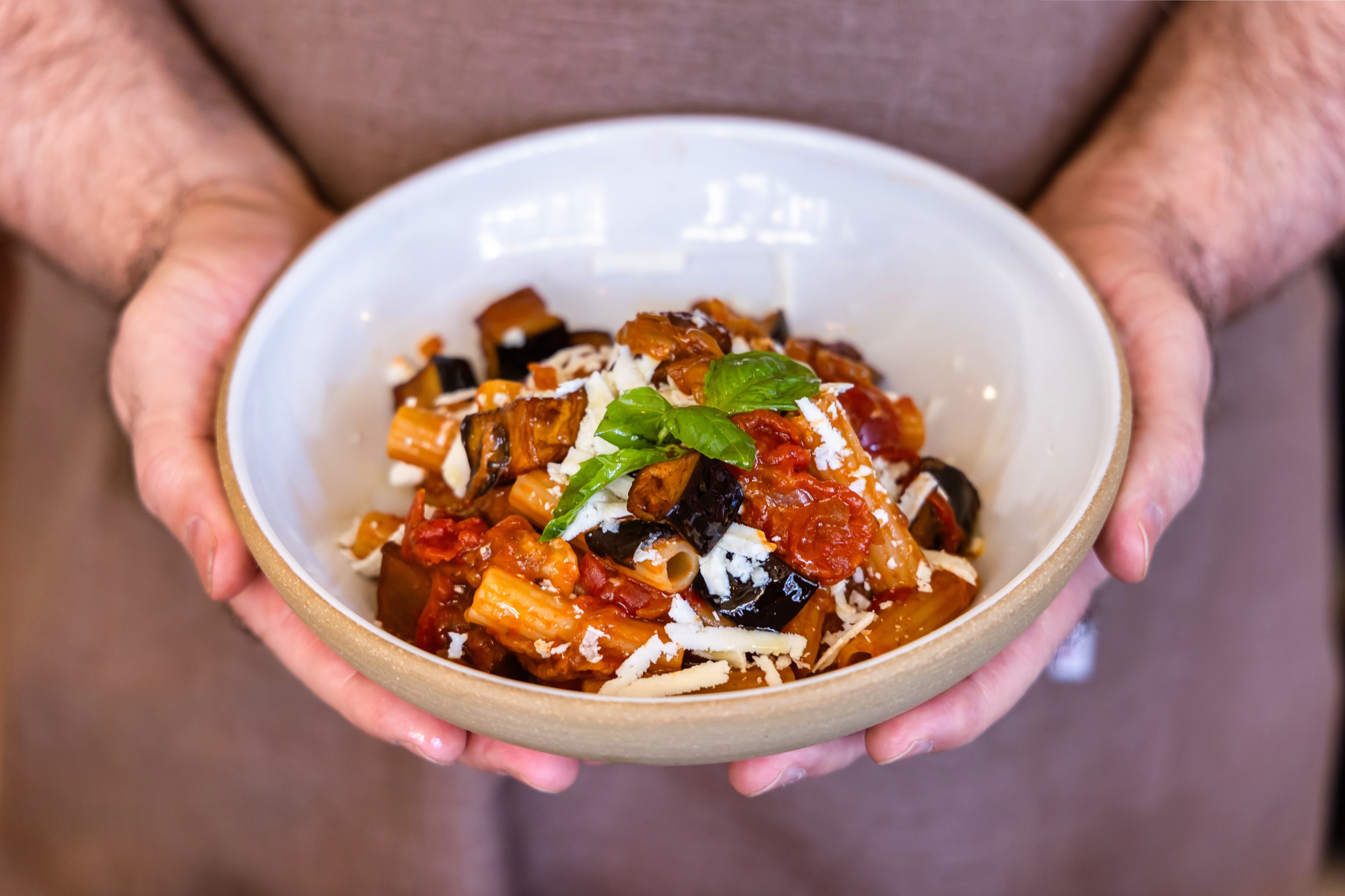 Pasta alla Norma with eggplant and tomato sauce in a white bowl held by a person's hands.