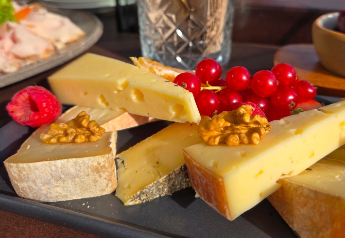 A cheeseboard with triangles of yellow cheese, fruit and nuts.