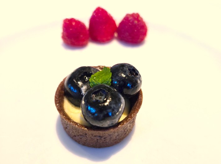 Crusted dessert topped with three blueberries and plated with raspberries on the side.