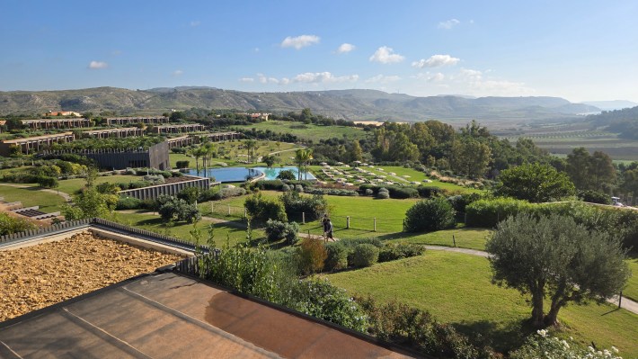 View of the pool, lawn and trees of the Adler Spa Resort SICILA, with mountains in background.
