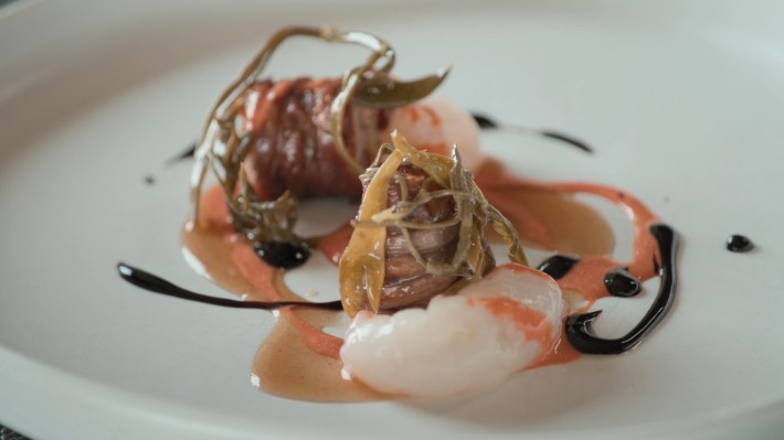 Seafood meal on white plate, drizzled with pepper sauce and olive oil.