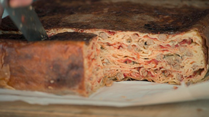 Timballo, layered crepes and mini meatballs, plated on a white plate and being cut into.