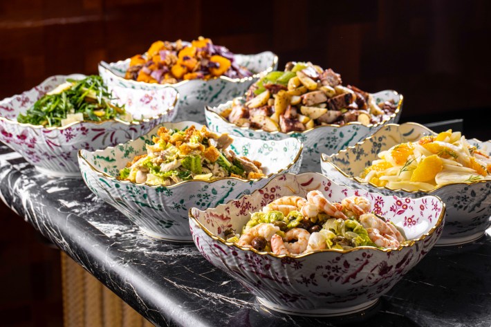 A variety of colorful Italian salads displayed in floral porcelain bowls on a marble counter