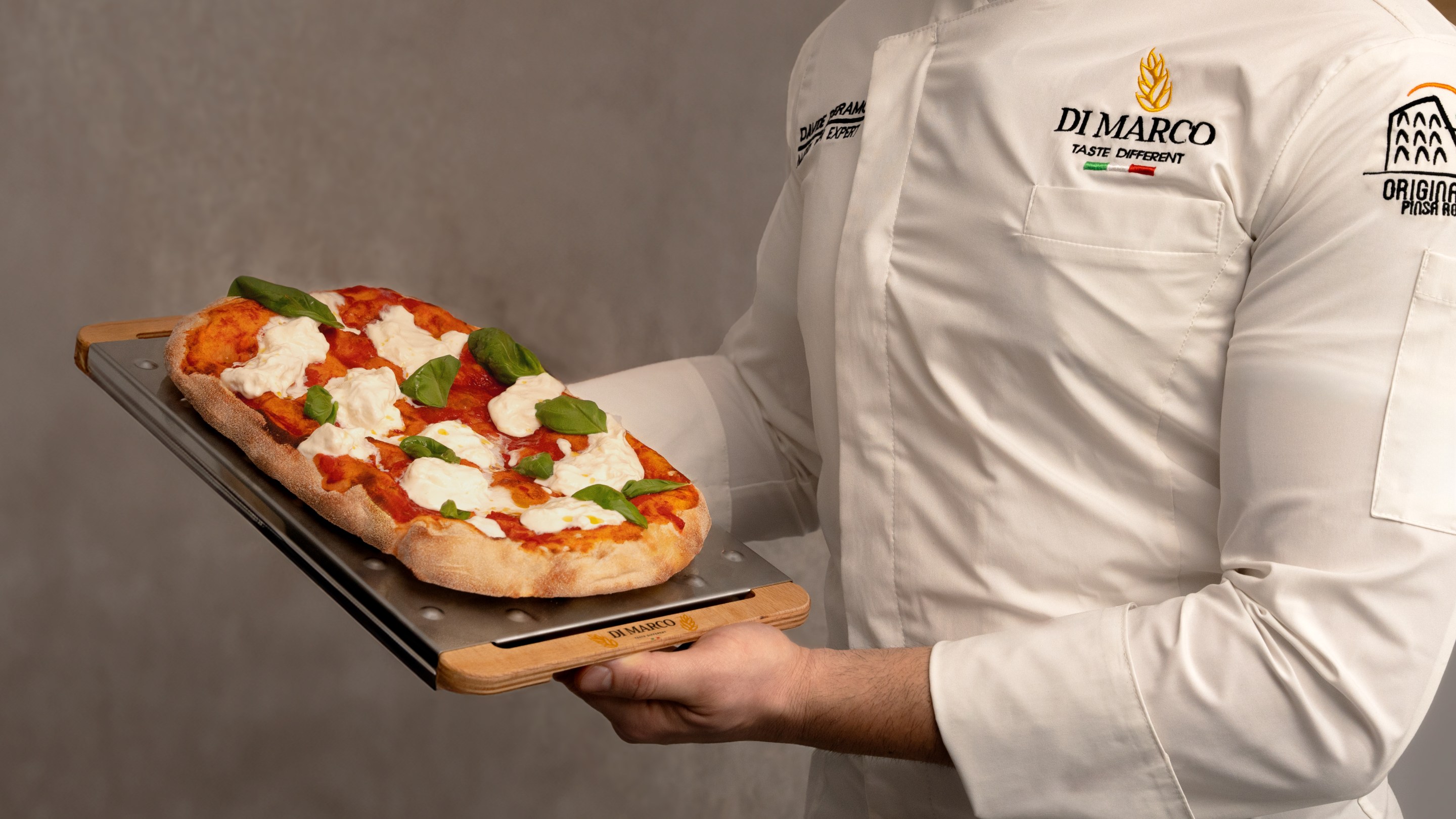 Chef holding a freshly baked pinsa with tomato and mozzarella
