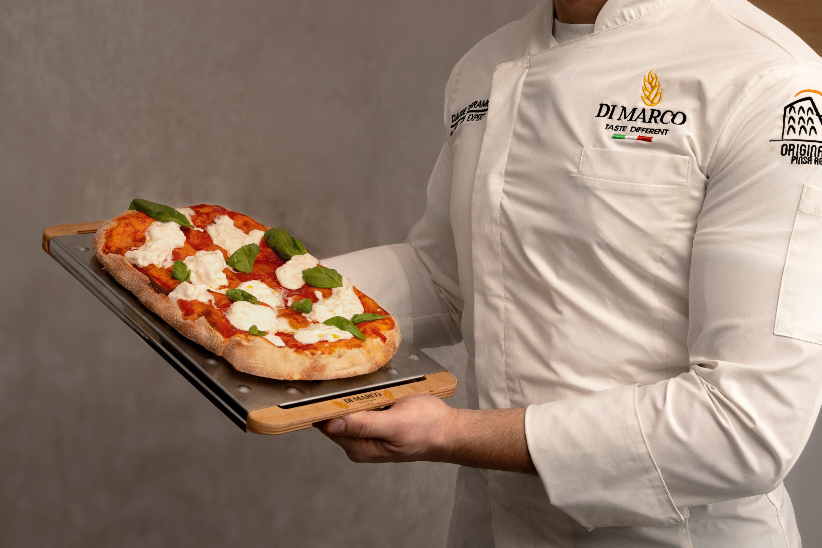 Chef holding a freshly baked pinsa with tomato and mozzarella