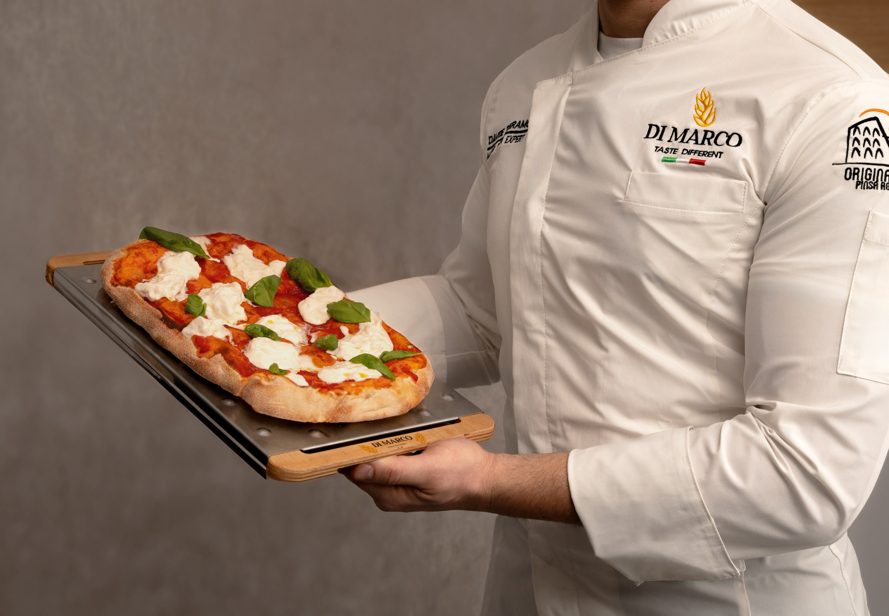 Chef holding a freshly baked pinsa with tomato and mozzarella