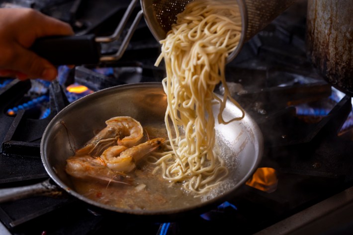 Fresh pasta being added to a sauté pan with shrimp