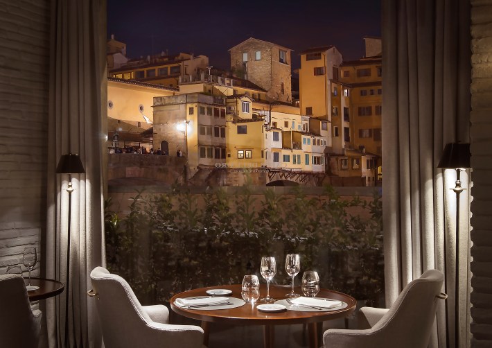 Elegant dining table set for two with a view of the illuminated Ponte Vecchio through a large window
