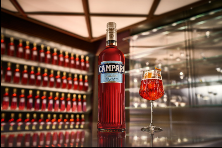 Bottle of Campari with a glass of Campari Spritz in a bar lined with red bottles