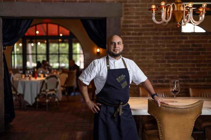 Chef Alex Espinoza standing in Bottega’s dining room beside a wine glass