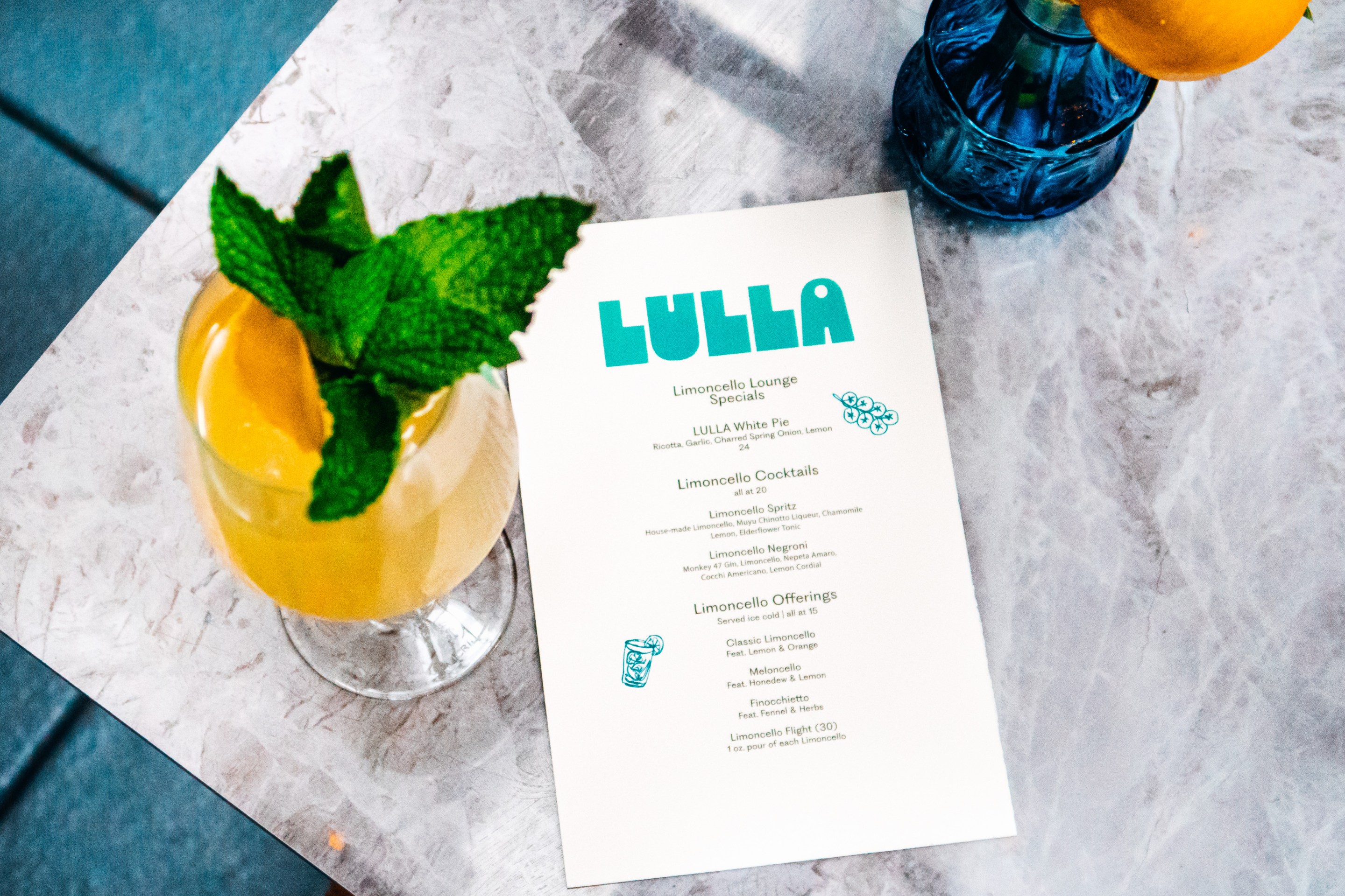 Close-up of a Limoncello Spritz next to Lulla’s printed menu on a marble table