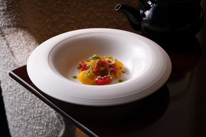 Bright yellow and red summer tomatoes served in a white bowl with herbs and a light sauce