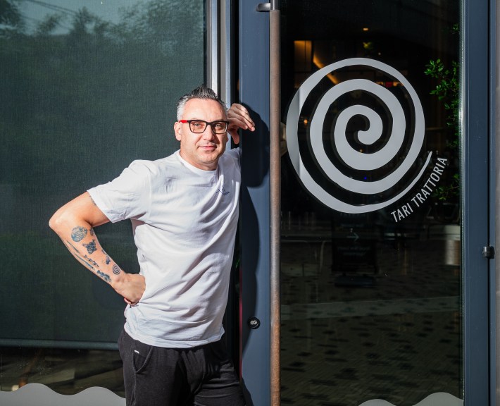 Francesco Amodeo in white shirt standing beside glass door with Tarì Trattoria logo