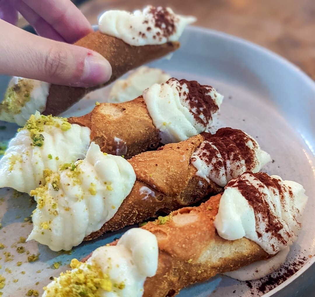 A plate of cannoli from Piccola Cucina, some dusted with cocoa and others with pistachios