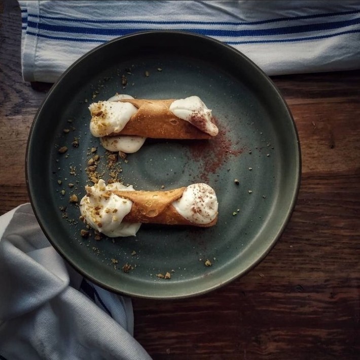 Overhead view of two cannoli on a green plate, garnished with cocoa powder and pistachio crumbs