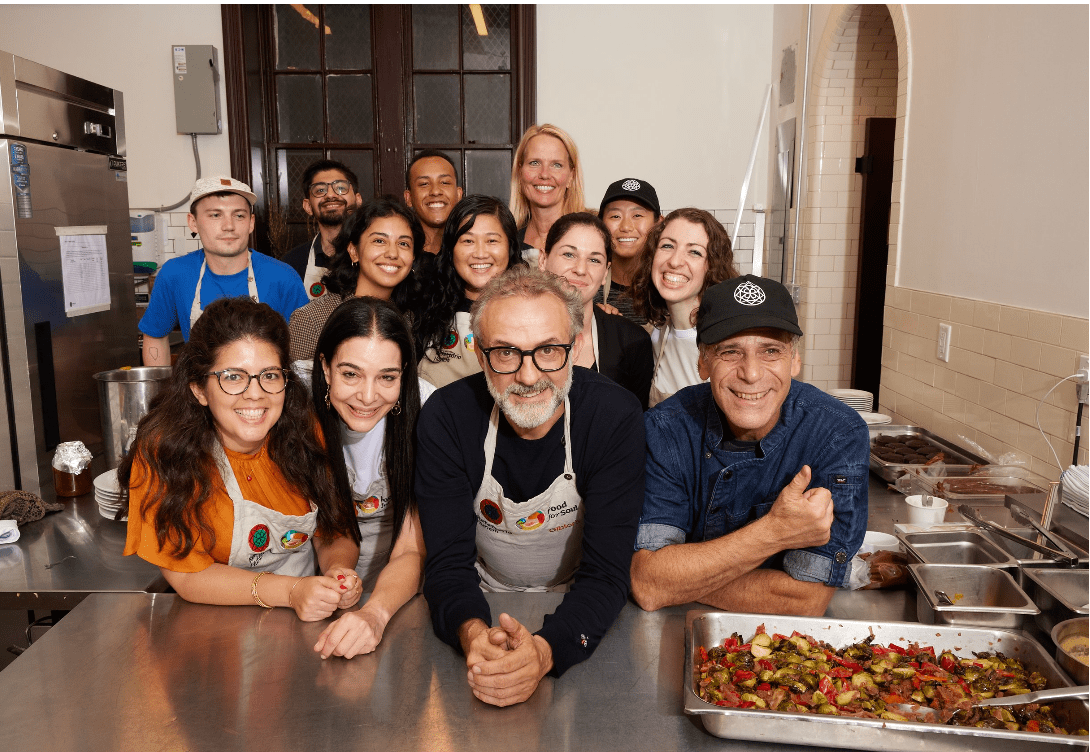 Massimo Bottura and the Refettorio Harlem team smiling in the kitchen during a meal service.