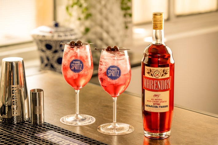 Two Marendry spritz cocktails garnished with Amarena cherries beside a bottle of Marendry.
