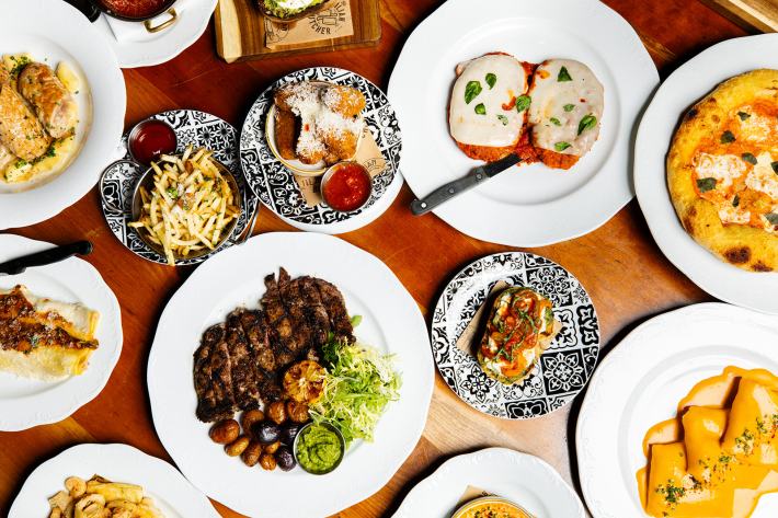 Italian dishes including steak, pasta, pizza, and appetizers on a wood table