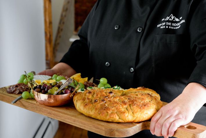 Chefin a Top of the Ridge chef coat holding a rustic focaccia and antipasto board