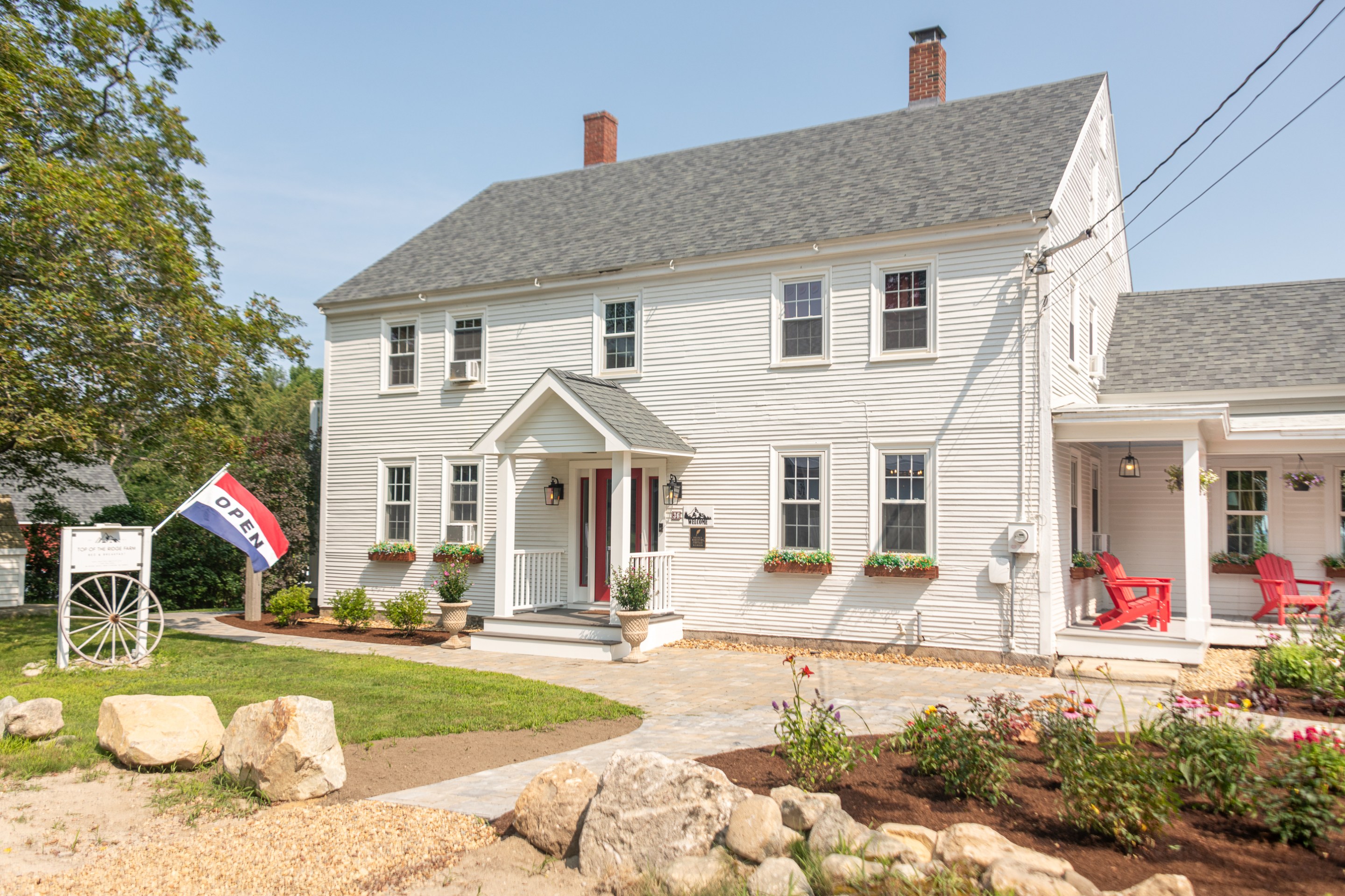 White farmhouse with red door and “Open” flag out front