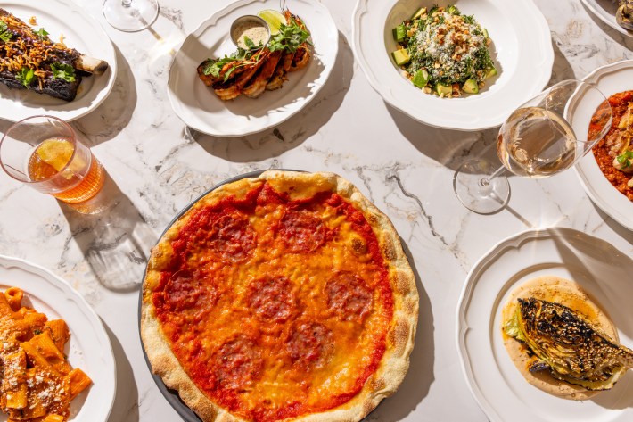Overhead view of a full Italian meal including pizza, pasta, wine, grilled vegetables, and seafood
