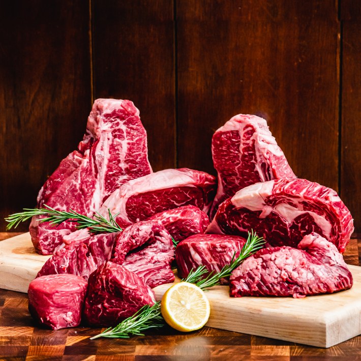 Four raw ribeye steaks with rosemary and lemon on a wooden cutting board