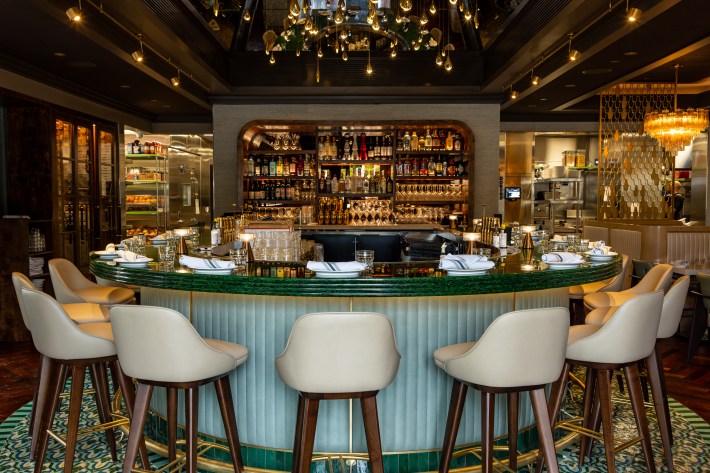 U-shaped bar with white barstools, place settings with white napkins, centered around a full bar and lighting.