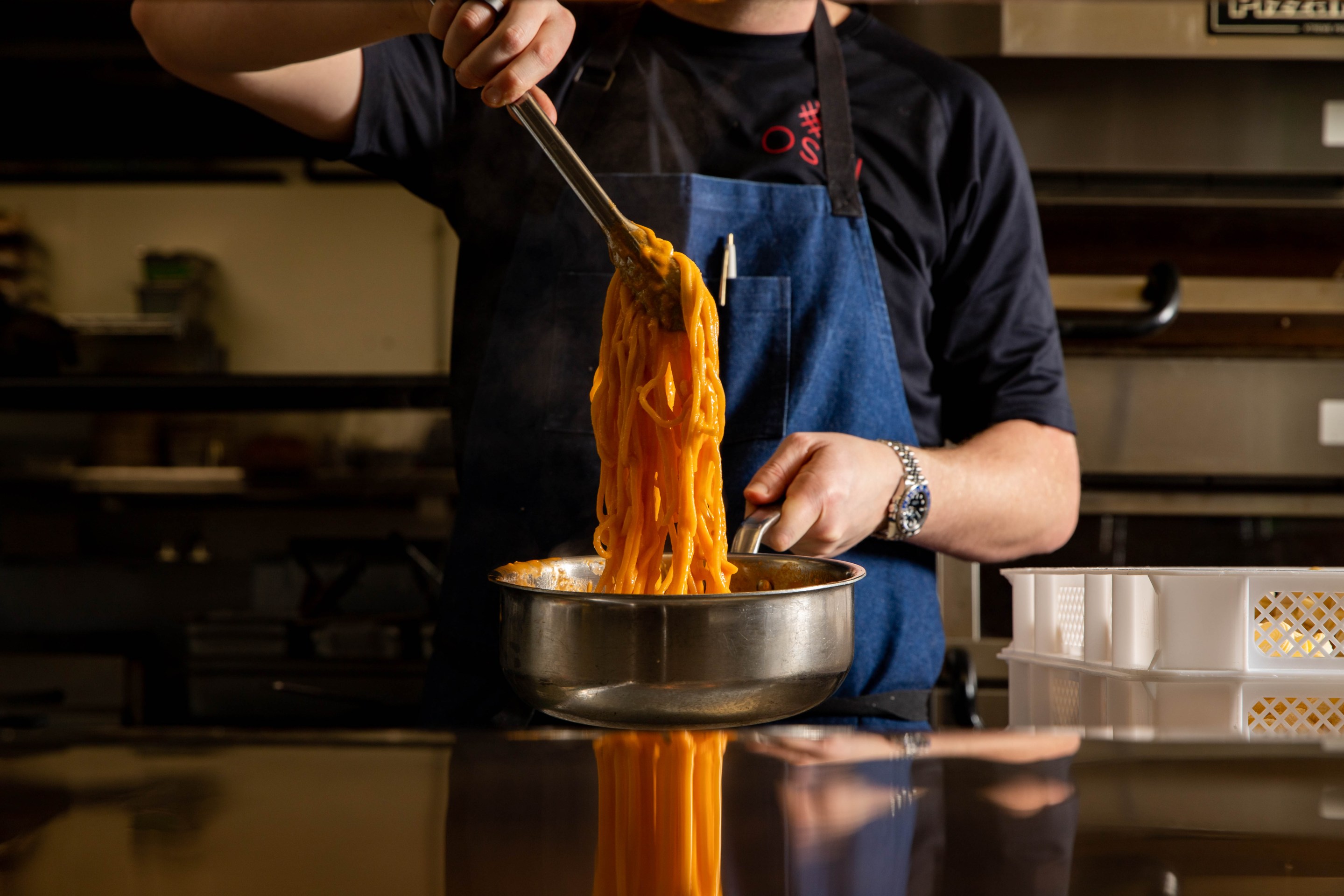 Chef cooking pasta in a blue apron and black shirt.