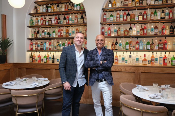 Two men smiling in front of liquor shelves at Johnny & Sanny’s restaurant