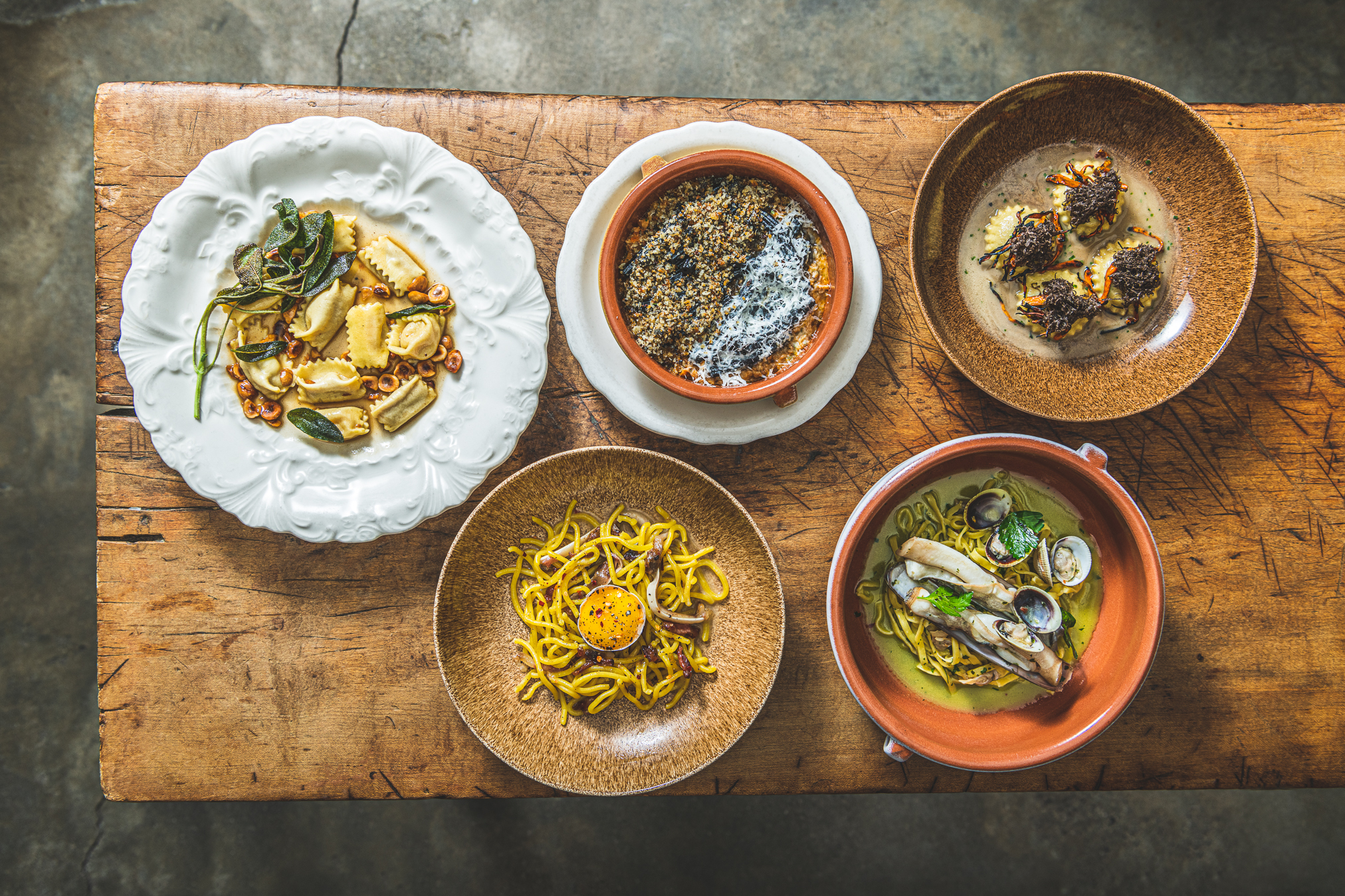Five plated pasta and grain dishes from Peasant displayed on a wooden table