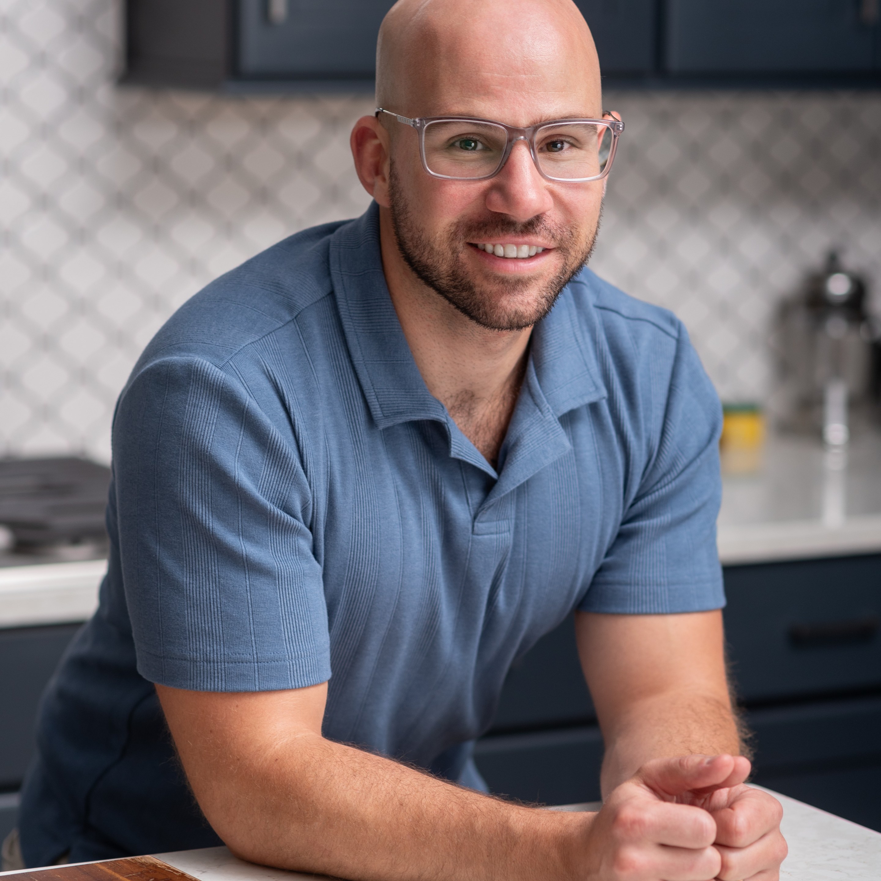 Vinny DelGiudice smiling in his kitchen, wearing a blue shirt and glasses.