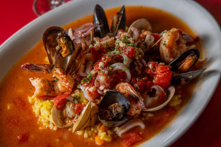 Bowl of saffron risotto topped with clams, mussels, shrimp, and tomatoes in broth at Asti Trattoria.