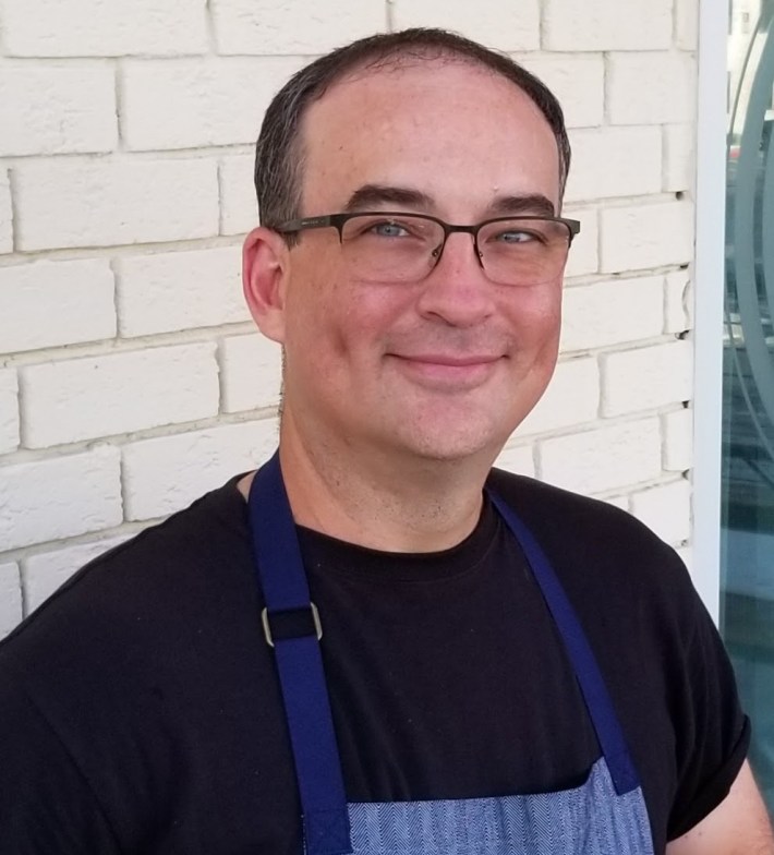Portrait of Chef Bryan Beneke in a black shirt and apron outside Asti Trattoria.