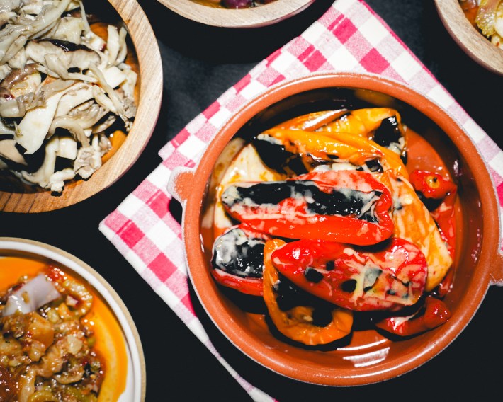 Bowls filled with roasted red and yellow peppers on a table with a red checkered towel.