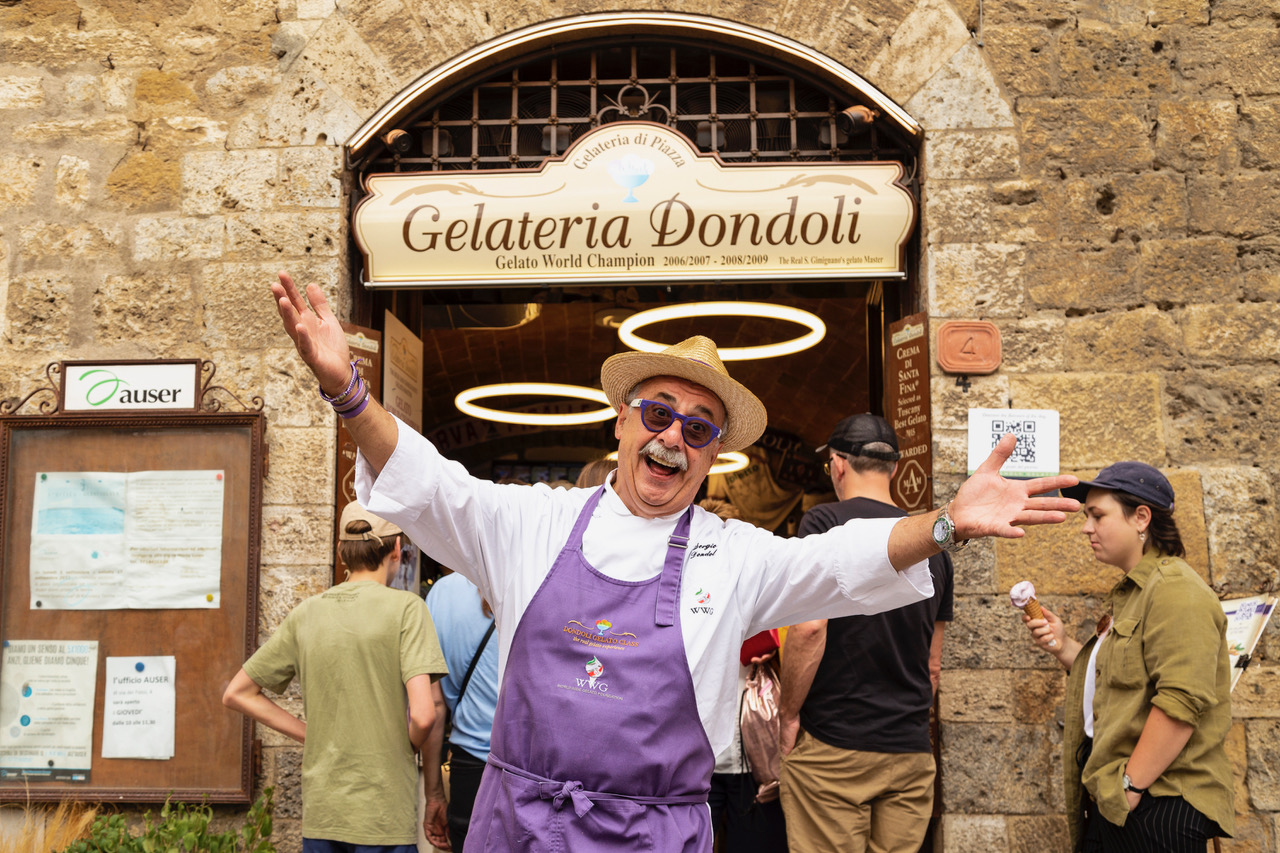 View of San Gimignano streets with gelato shop signs and passing visitors.